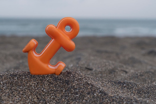 Foto nahaufnahme eines kleinen orangefarbenen anker-strandspielzeugs, das auf dem schwarzen sand am batu bolong-strand platziert ist