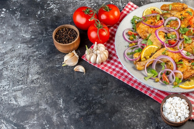 Nahaufnahme eines köstlichen gebratenen Hühnchengerichts mit verschiedenen Gewürzen und Lebensmitteln Tomaten mit Stielen Pfeffer Zwiebeln Knoblauch Salz auf der linken Seite auf dunklem Hintergrund