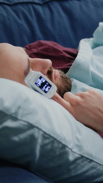 Nahaufnahme eines kranken Mannes, der auf dem Sofa mit Oximeter am Finger schläft