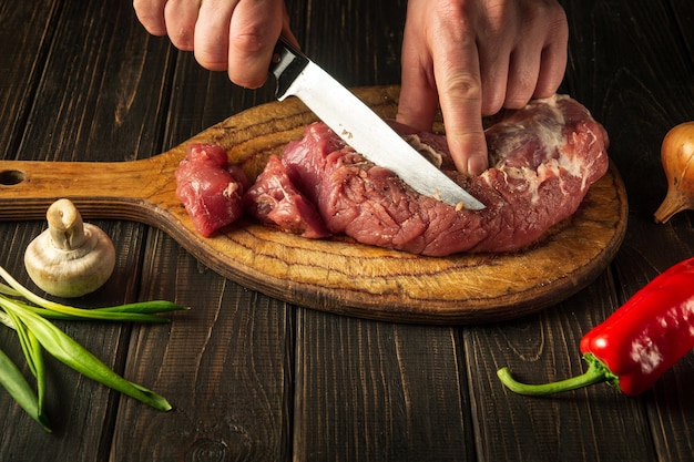 Nahaufnahme eines Küchenchefs, der rohes Kalbfleisch auf einem Schneidebrett schneidet, bevor er bäuerliche Lebensmittel kocht