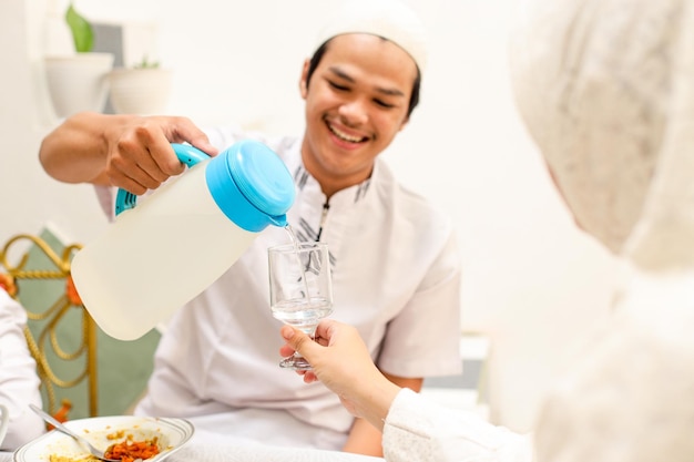 Nahaufnahme eines lächelnden jungen muslimischen mannes, der seiner schwester im speisesaal während eid mubarak wasser serviert