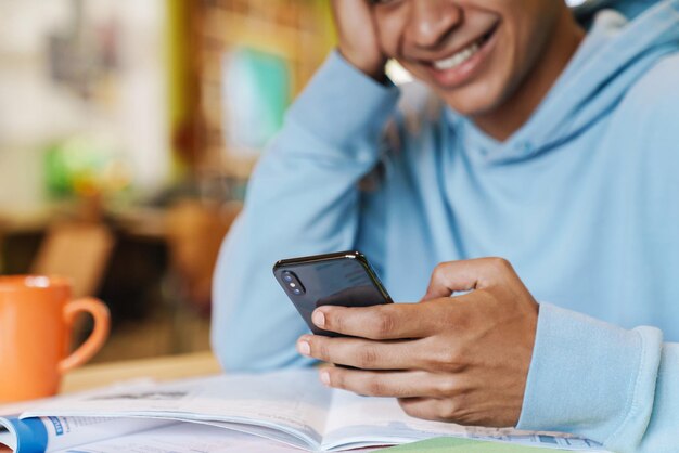 Nahaufnahme eines lächelnden jungen Teenagers, der lernt, während er drinnen am Hub sitzt, mit Handy