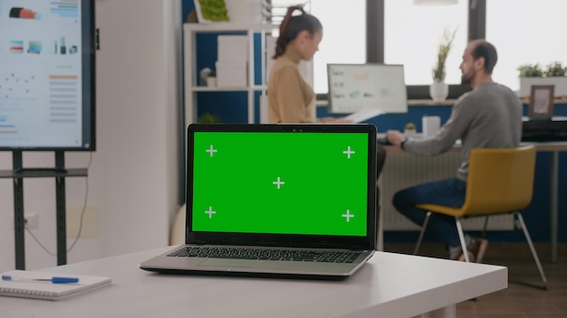 Nahaufnahme eines Laptops mit grünem Bildschirm auf einem leeren Schreibtisch. Isolierte Vorlage und Mock-up-Kopienraumhintergrund auf dem Computerdisplay mit Chroma-Key. Digitale Mockup-App auf dem Bildschirm.