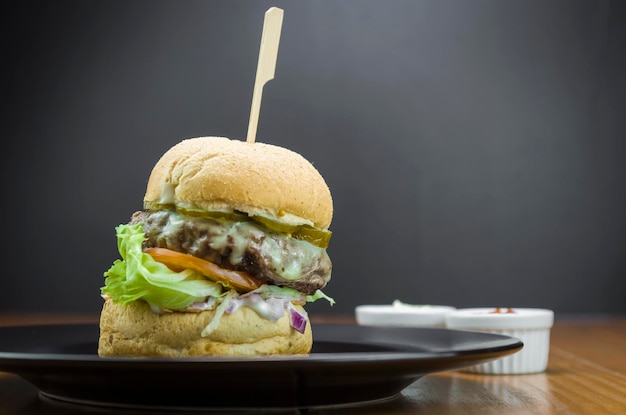 Nahaufnahme eines leckeren hausgemachten Hamburgers auf Holztisch und schwarzem Hintergrund