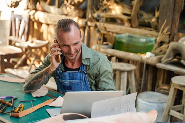 Nahaufnahme eines Lederhandwerkers, der mobil mit dem Kunden über Bestellungen im Online-Shop mit Laptop spricht