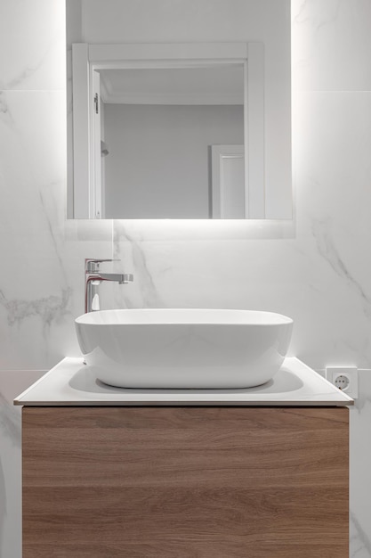 Nahaufnahme eines leeren Badezimmers in Weißtönen mit einem Waschbecken mit Schrank und einem neuen Spiegel