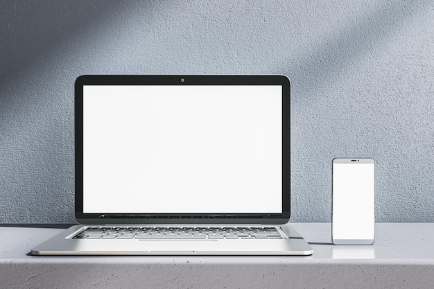 Nahaufnahme eines leeren weißen Laptops und Smartphones auf einem grauen Schreibtisch Betonwand-Hintergrund Gerätpräsentation und Online-Bildungskonzept Mock-up 3D-Rendering