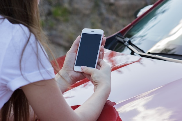 Nahaufnahme eines Mädchens, das einen Smartphone auf der Haube eines Autos hält