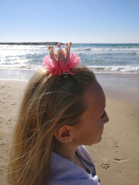 Foto nahaufnahme eines mädchens mit einem kronenhaarklemmen, das auf den strand blickt