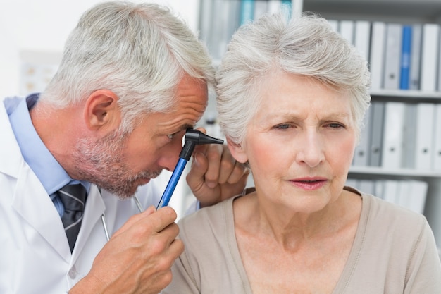 Nahaufnahme eines männlichen Doktors, der das Ohr des älteren Patienten überprüft