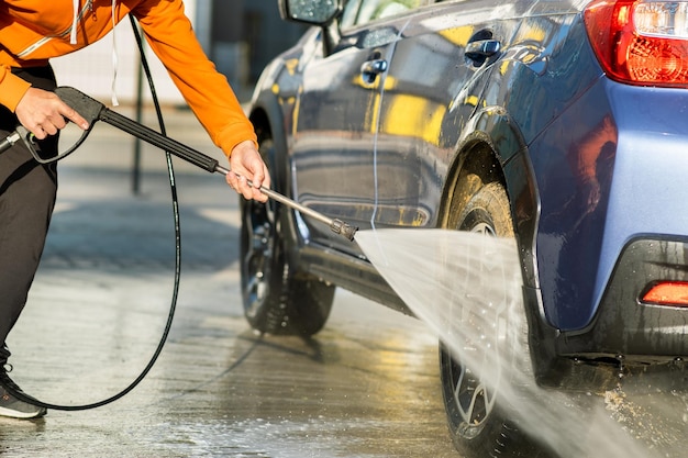 Nahaufnahme eines männlichen Fahrers, der sein Auto mit kontaktlosem Hochdruckwasserstrahl in der Selbstbedienungswaschanlage wäscht