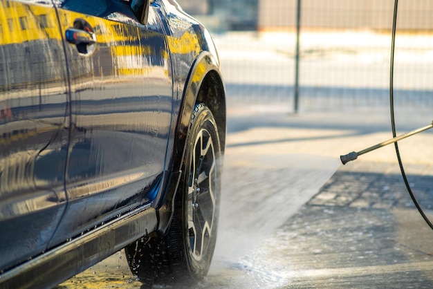 Nahaufnahme eines männlichen Fahrers, der sein Auto mit kontaktlosem Hochdruckwasserstrahl in der Selbstbedienungswaschanlage wäscht