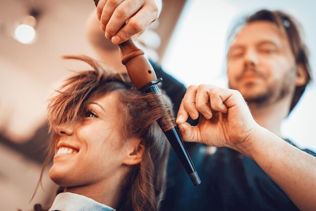 Nahaufnahme eines männlichen Friseurs, der Locken an langen braunen Haaren mit Lockenstäben macht.