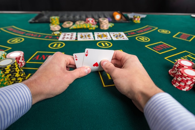 Nahaufnahme eines männlichen Pokerspielers, der die Ecken von zwei Karten-Assen am grünen Casino-Tisch mit Assen anhebt