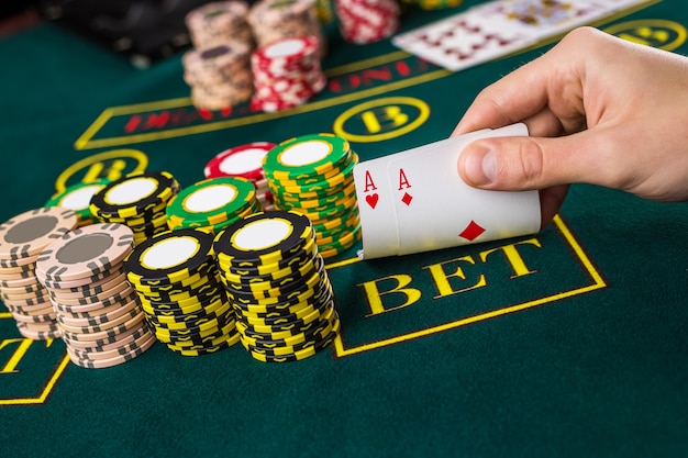 Nahaufnahme eines männlichen Pokerspielers, der die Ecken von zwei Karten-Assen am grünen Casino-Tisch mit Assen anhebt