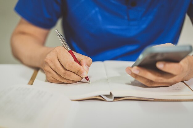 Nahaufnahme eines männlichen Studenten, der zu Hause vom Lernen auf einem Smartphone Notiz nimmt