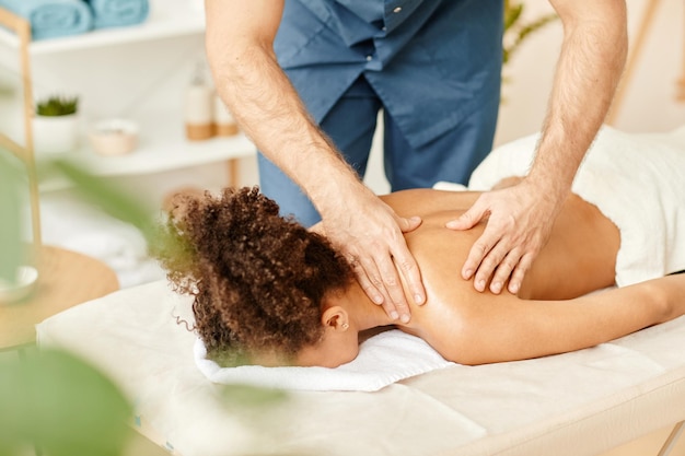 Nahaufnahme eines männlichen Therapeuten, der einer jungen afroamerikanischen Frau, die eine Spa-Sitzung genießt, eine Rückenmassage gibt