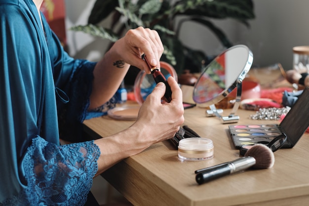 Nahaufnahme eines Mannes, der am Tisch sitzt und während der Vorbereitung auf die Aufführung Lippenstift im Make-up verwendet