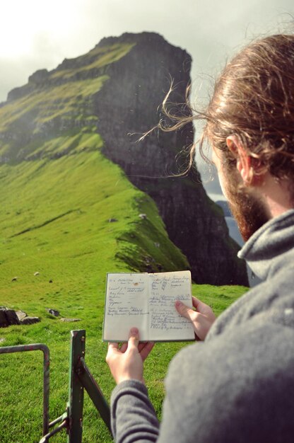 Nahaufnahme eines Mannes, der an einem sonnigen Tag auf einem grasbewachsenen Berg ein Buch liest