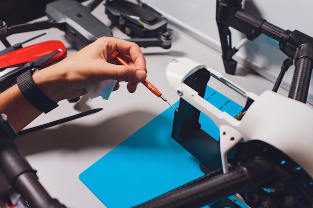 Foto nahaufnahme eines mannes, der bei der montage eines neuen überwachungssystems mit einer quadcopter-drohne mit kamera auf dem tisch mit verschiedenen werkzeugen in einer modernen werkstatt arbeitet