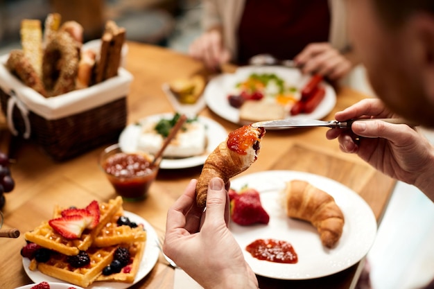 Nahaufnahme eines Mannes, der Croissants mit Marmelade zum Frühstück isst