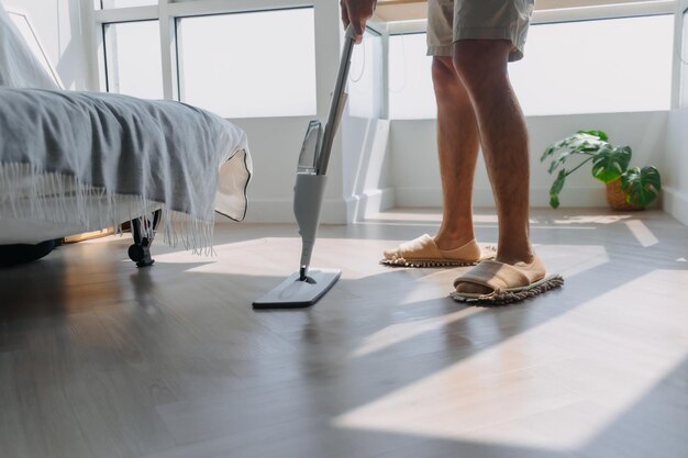 Nahaufnahme eines Mannes, der die Beine mit der Hand hält und den Mopp benutzt, um den Boden in der Wohnzimmerwohnung zu reinigen.