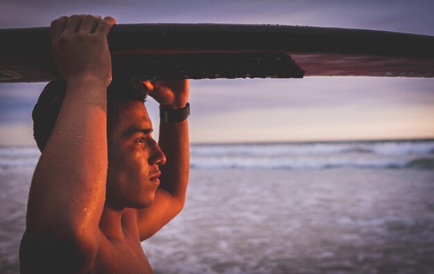 Foto nahaufnahme eines mannes, der ein surfbrett auf dem kopf trägt, während er am strand steht