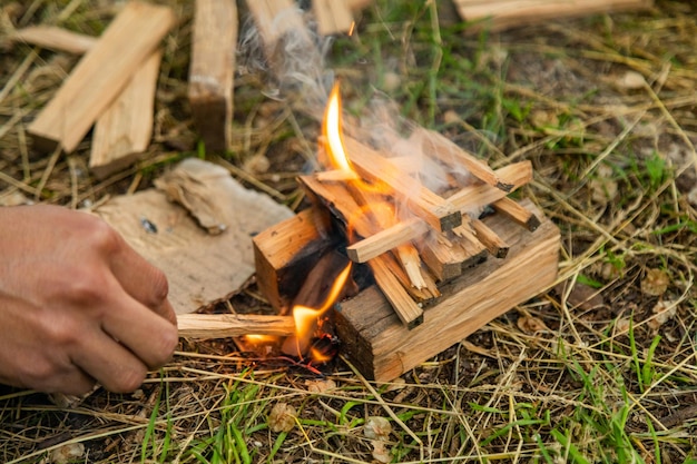 Nahaufnahme eines Mannes, der Holzstücke anzündet, die als Brennholz gehackt wurden und auf dem Boden liegen