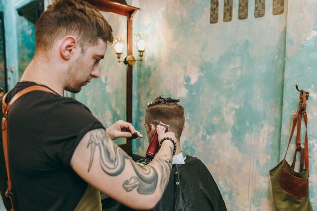 Nahaufnahme eines Mannes, der im Friseurladen einen trendigen Haarschnitt erhält. Der männliche Friseur in Tätowierungen, der dem Kunden dient.