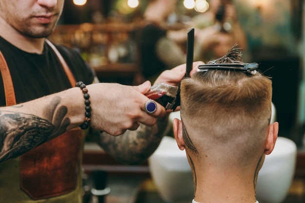 Nahaufnahme eines Mannes, der im Friseurladen einen trendigen Haarschnitt erhält. Der männliche Friseur in Tätowierungen, der dem Kunden dient.