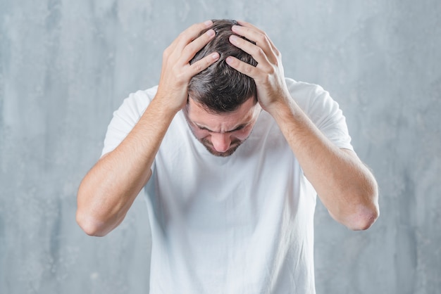 Nahaufnahme eines Mannes, der unter Kopfschmerzen gegen grauen Hintergrund leidet