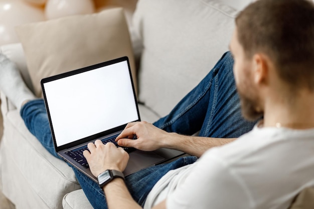 Nahaufnahme eines Mannes, der zu Hause an einem Laptop auf der Couch arbeitet, kein Gesicht