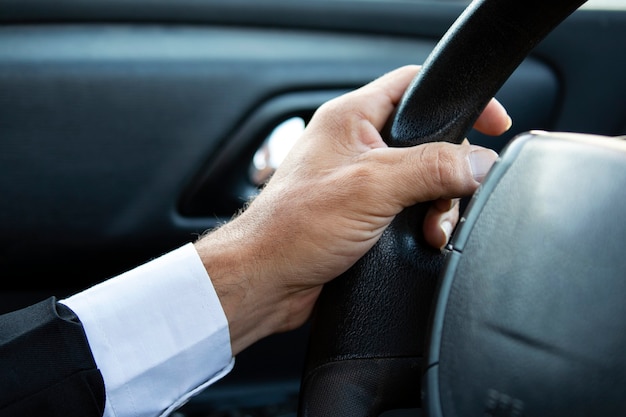 Nahaufnahme eines Mannes Hände halten Lenkrad beim Autofahren. Geschäftsmann während der Fahrt, beschnitten. Die Hand des Fahrers am Lenkrad im Anzug. Kerl sitzt im Auto und hält die Hände am Lenkrad