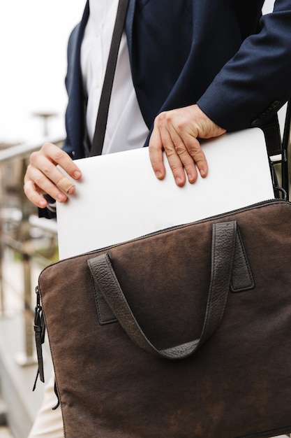 Nahaufnahme eines Mannes in formeller Kleidung, der seinen Laptop aus der Tasche nimmt, während er im Freien steht