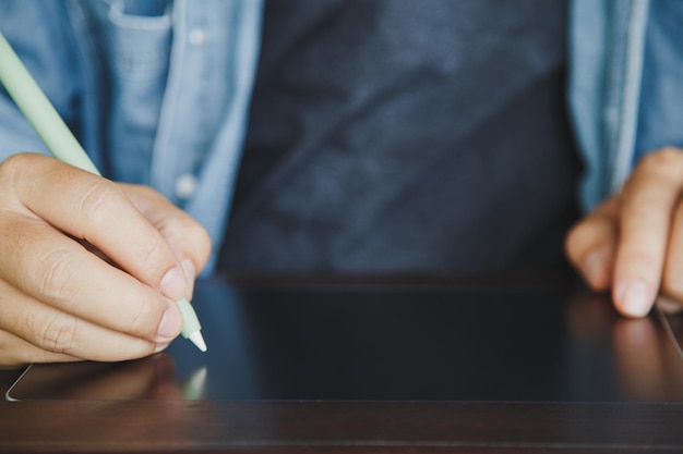 Nahaufnahme eines Mannes in Freizeitkleidung mit einem elektronischen Stift auf einem leeren Tablet auf dem Holztisch