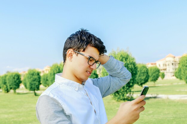 Nahaufnahme eines Mannes mit Mobiltelefon auf dem Gras gegen den Himmel