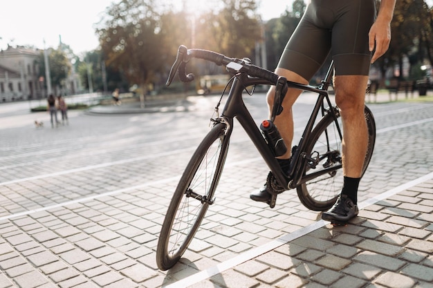 Nahaufnahme eines Mannes mit muskulösen Beinen, der auf einem schwarzen Fahrrad unter den kaukasischen Radfahrern der Stadt sitzt, die sich während des Trainings im Freien entspannen Aktives Lebensstilkonzept