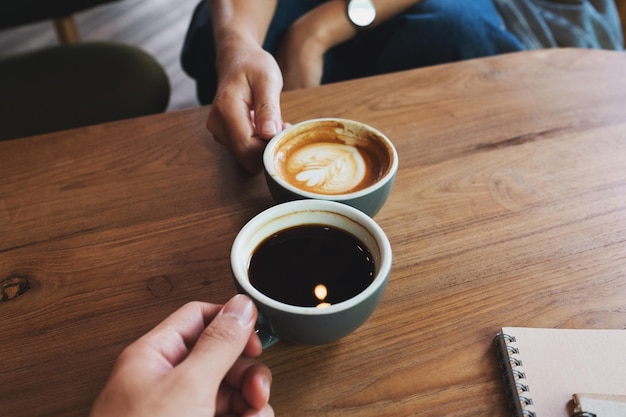 Nahaufnahme eines Mannes und einer Frau, die im Café mit weißen Kaffeetassen klirren