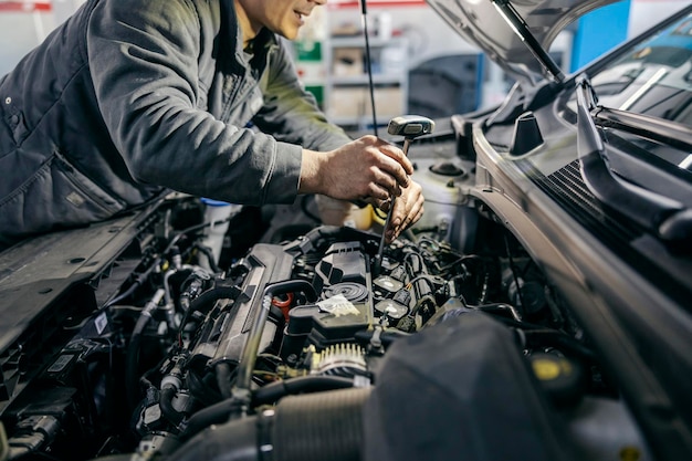 Nahaufnahme eines Mechanikers, der das Auto unter der Motorhaube mit Werkzeugen in der Garage repariert