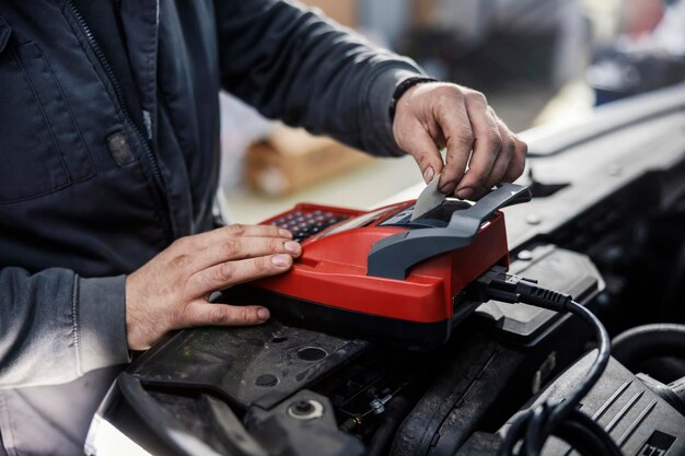 Nahaufnahme eines Mechanikers, der ein Gerät zur Überprüfung der Autobatterie verwendet