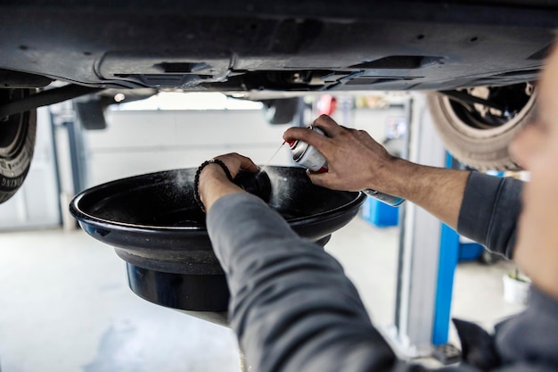 Nahaufnahme eines Mechanikers, der Rost am Motorteil reinigt, während das Öl aus dem Motor abgelassen wird