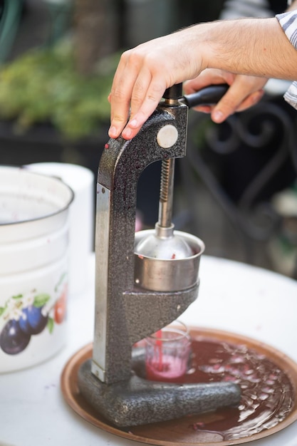 Nahaufnahme eines mechanischen Entsafters aus Eisen, der Granatapfel- oder Tomatensaft in einen Glasbecher drückt