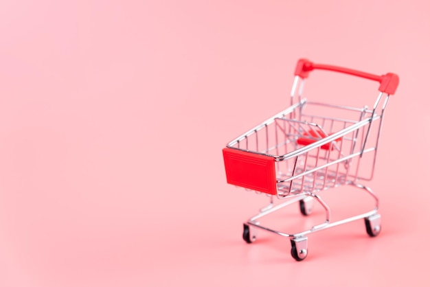 Nahaufnahme eines Miniatur-Einkaufswagens vor rosa Hintergrund