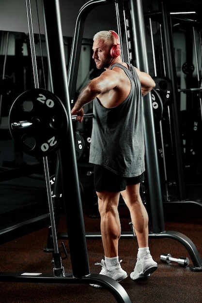 Nahaufnahme eines muskulösen Mannes, der im Fitnessstudio mit Langhantel trainiert. Brutaler Bodybuilder, athletischer Mann mit Sixpack, perfekten Bauchmuskeln, Schultern, Bizeps, Trizeps und Brust