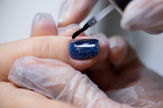 Nahaufnahme eines Nagels, auf den ein blauer Gellack aufgetragen wird, der mit einem Manikürpinsel über die Oberfläche verteilt wird