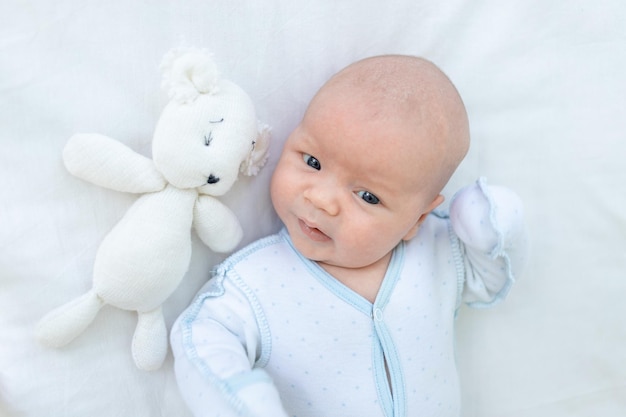 Nahaufnahme eines neugeborenen Jungen, der zu Hause auf dem Rücken eines Kinderbetts auf einem Baumwollbett liegt, bevor er mit einem weichen Spielzeug ins Bett geht, das Konzept der Geburt und Kindheit