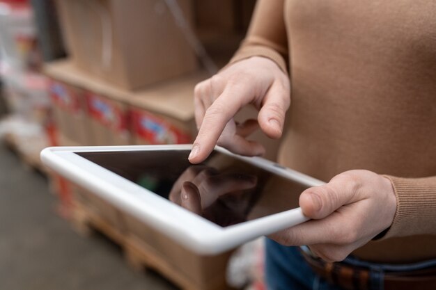 Foto nahaufnahme eines nicht erkennbaren lagerleiters in braunem pullover mit tablet, während die festgelegte anzahl von waren im lager analysiert wird