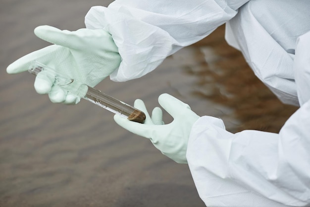 Nahaufnahme eines nicht erkennbaren Wissenschaftlers, der einen Hazmat-Anzug trägt und Wassersonden sammelt, konzentriert sich auf behandschuhte Han...