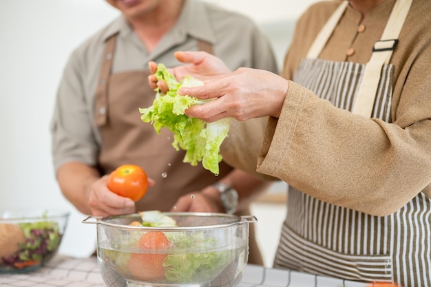Nahaufnahme eines Paares, bei dem Ehemann und Frau zusammen in der Küche eine Salatschüssel zubereiten