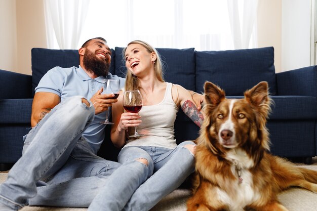 Nahaufnahme eines Paares, das Wein auf dem Sofa mit ihrem Border-Collie-Hund in der Nähe trinkt